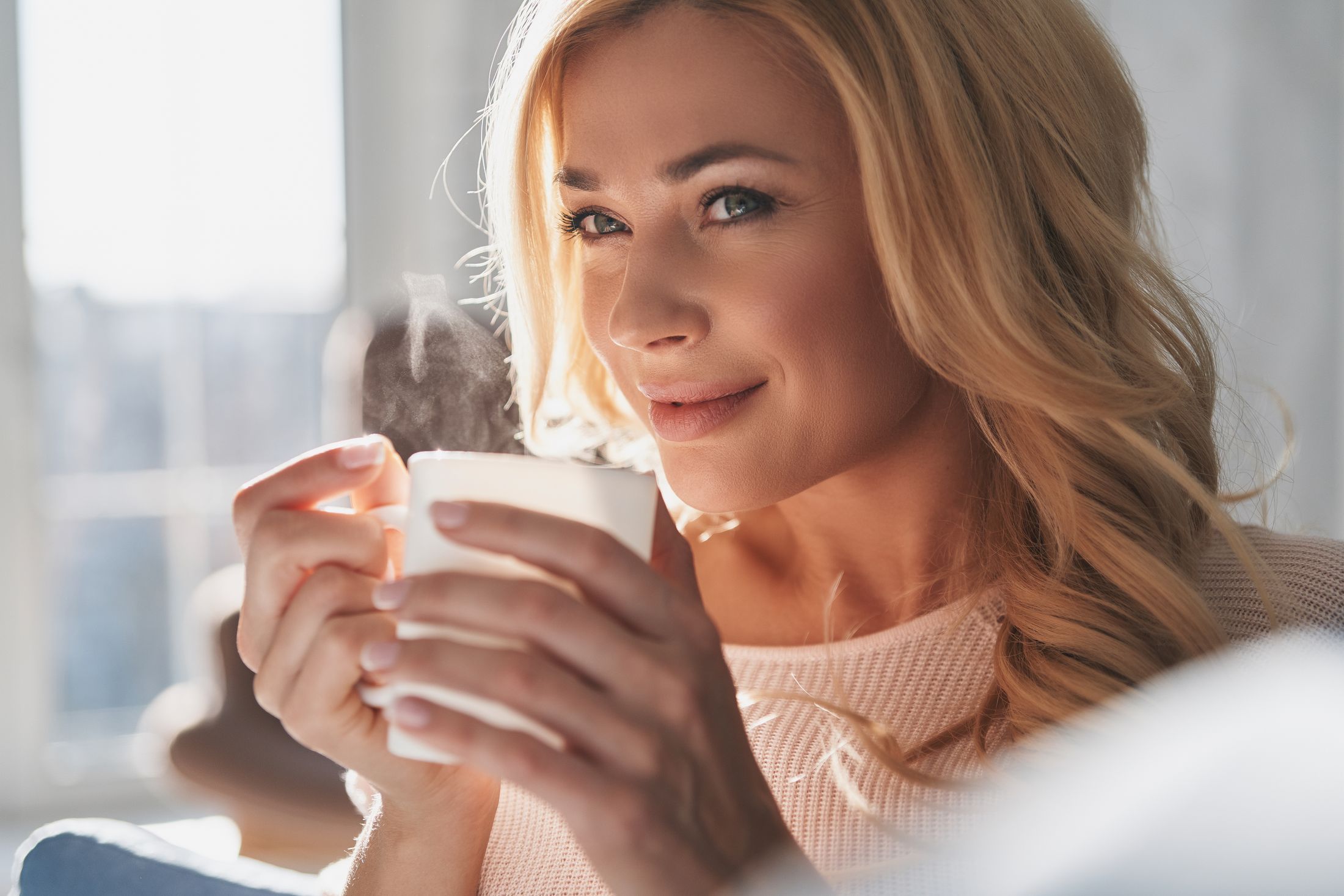 signature facial patient model holding a cup of coffee on the couch and smiling